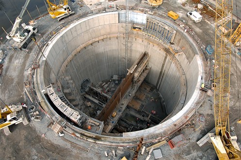 Benzene tunnelling Aerial view of a massive, circular, vertical shaft under construction. It is lined with concrete, and surrounded by cranes, bulldozers and other equipment. It is about 60 metres in diameter and almost as deep, and more construction equipment can be seen. A horizontal tunnel can be seen near the bottom, leading off from one side of the shaft into the surrounding ground It is a demonstration of Benzene tunnelling